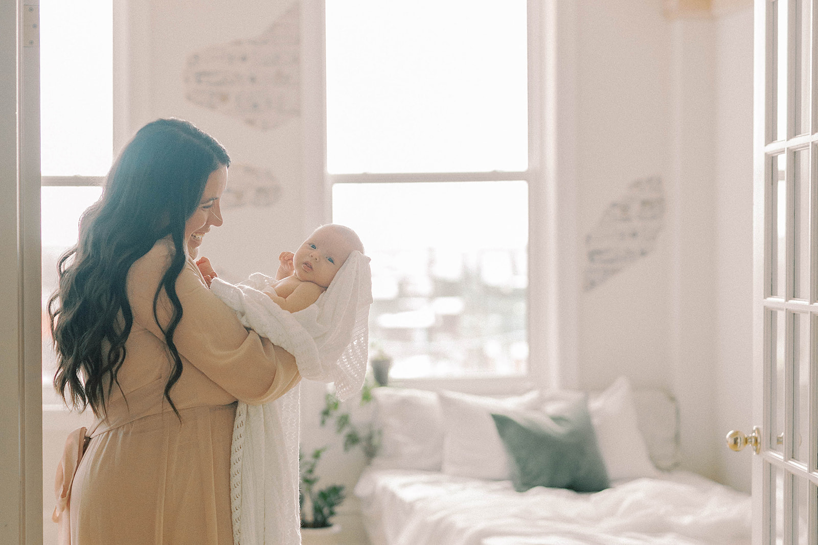mother standing in doorway holding baby wrapped in white blanket